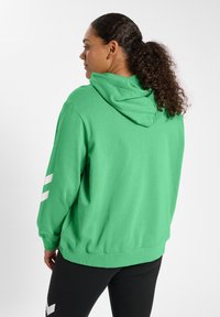 Grön hoodie med avslappnad passform, med en stor huva och vita ränder på ärmarna. Materialet ser mjukt ut med en texturerad look.