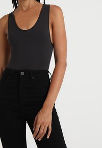 Svart ribbad bodysuit med rund halsringning, i kombination med höga svarta jeans med knappstängning och framfickor.