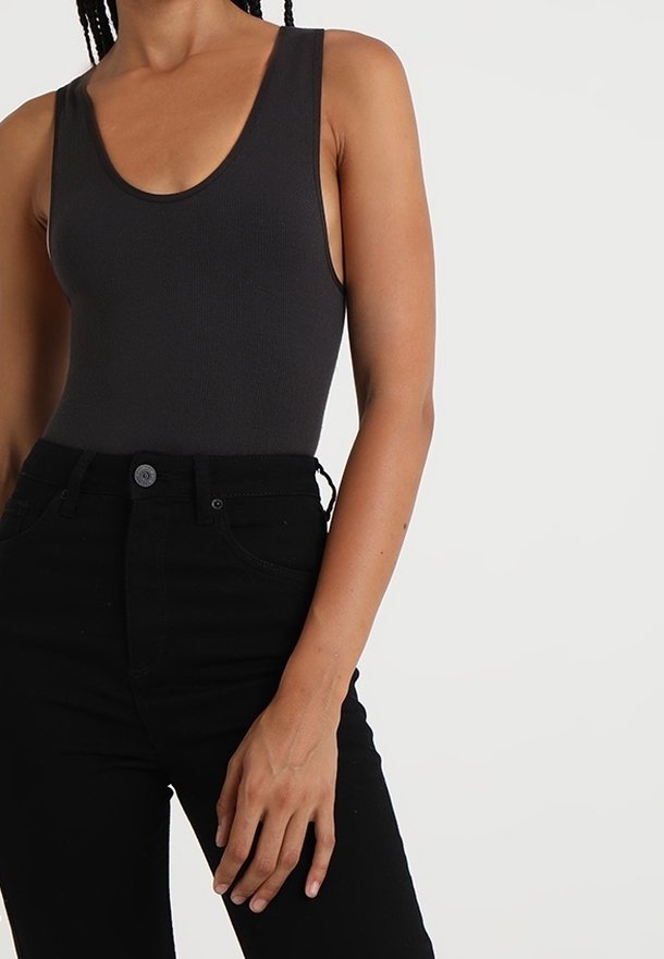 Svart ribbad bodysuit med rund halsringning, i kombination med höga svarta jeans med knappstängning och framfickor.