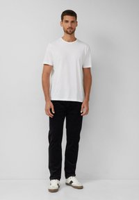 Biała bawełniana koszulka z okrągłym dekoltem, w zestawieniu z czarnymi spodniami sztruksowymi i białymi trampkami z czarnymi akcentami.