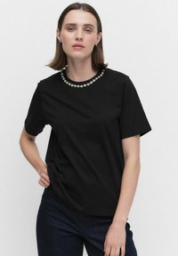 Svart bomull T-shirt med korta ärmar och rund krage prydd med dekorativa blommiga utsmyckningar runt halsringningen.