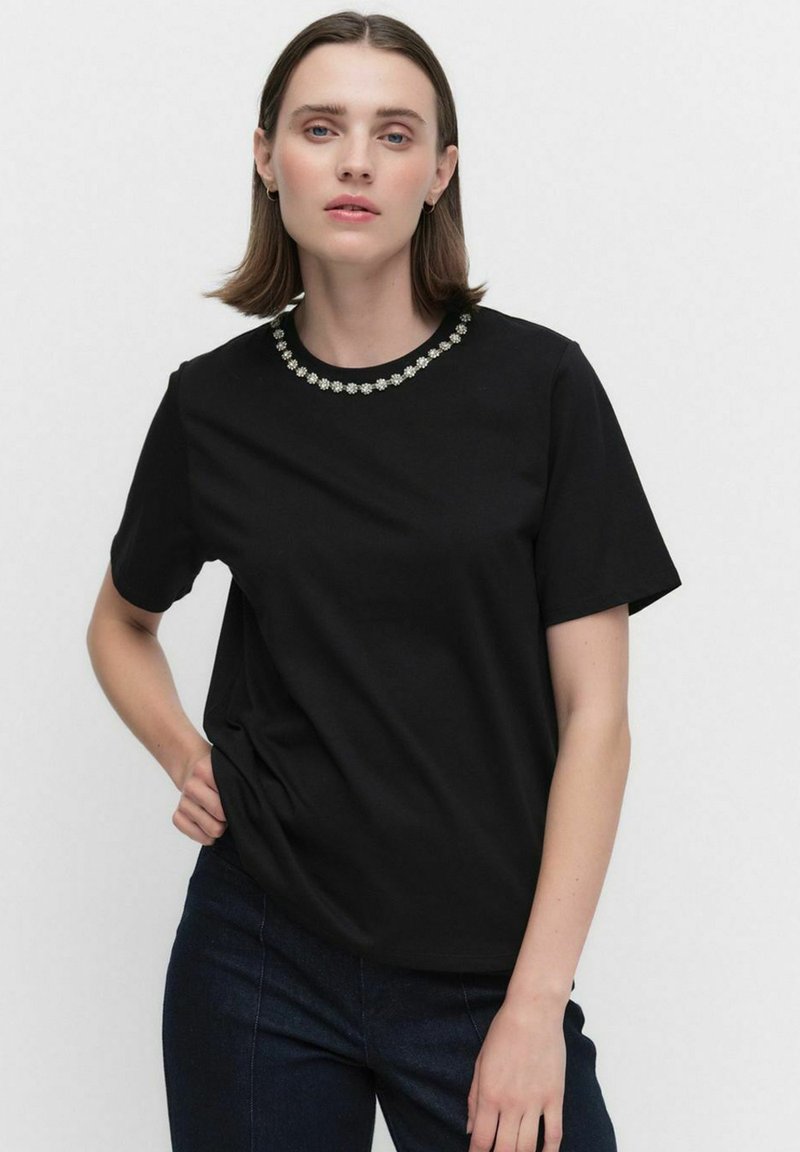 Svart bomull T-shirt med korta ärmar och rund krage prydd med dekorativa blommiga utsmyckningar runt halsringningen.