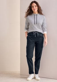 Stribet langærmet top i hvid og marineblå, parret med mørke cargo bukser med sidelommer og snoreliv, båret med hvide sneakers.