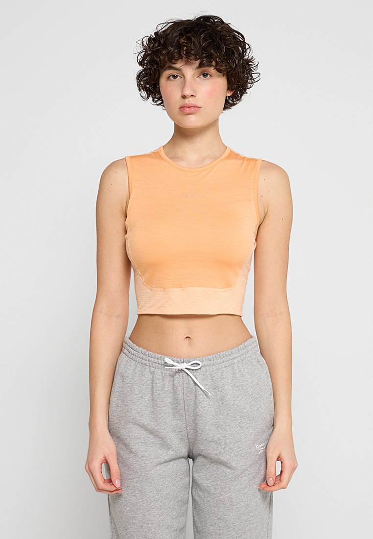 Brzoskwiniowy crop top z miękkiego materiału, z okrągłym dekoltem i bez rękawów, w zestawie z szarymi spodniami dresowymi ze sznurkiem do ściągania.