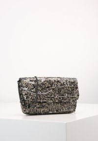 Borsetta a pochette in sequins metallici con design piegato. Presenta una tracolla attorcigliata. Predominantemente argento e nero con diverse textures.