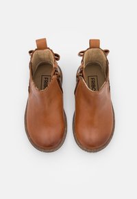 Bottines en cuir marron avec une texture lisse, bout arrondi et semelle basse texturée. Équipées de fermetures zippées sur le côté et d'une boucle au talon.