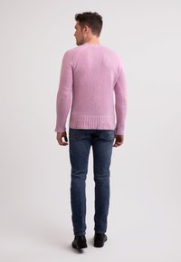 Maglione rosa a maglia con polsini e orlo a coste, abbinato a jeans blu scuro. Il maglione ha un collo rotondo e una vestibilità senza cuciture sulle spalle.