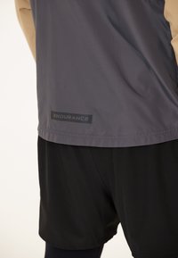 Sportbekleidungsset mit einem grauen, leichten, strukturierten Oberteil und schwarzen Shorts. Das Oberteil hat ein schwarzes "ENDURANCE"-Label am Saum.