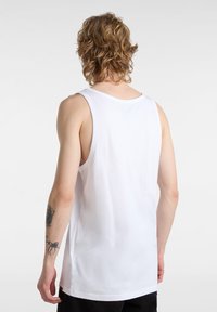 Top de algodón blanco sin mangas con escote redondeado y dobladillo recto. Presenta una textura suave y un estilo minimalista.