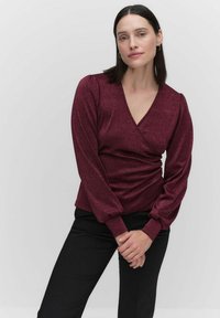 Burgundy, kimono-hihainen, V-päinen ja kootuilla puffihihnoilla varustettu toppi, yhdistetty mustiin housuihin. Sujuva pinta korostaa kiiltoa.