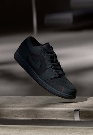 Czarny sneaker Nike z sznurówkami unoszący się nad betonową powierzchnią w słabym świetle i zacienionym tle.