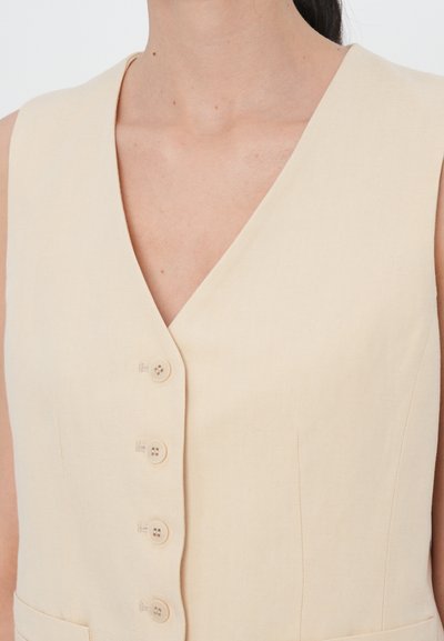 Beige liininivestimekko syvällä V-muotoisella kaula-aukolla, jossa on kuusi nappia edessä ja sivutaskut, sileä pinta ja minimalistinen muotoilu.