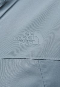 Ανοιχτό μπλε ύφασμα με ομαλή υφή, που φέρει ένα ανάγλυφο, λευκό λογότυπο του "THE NORTH FACE" στην κάτω δεξιά γωνία.