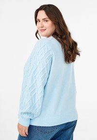 Ljusblått stickat tröja med texturerade ärmar med diamantmönster och ribbat avslut. Matchas med mörkblå jeans.