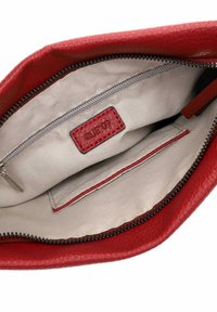 Intérieur d'un sac à main en cuir rouge avec une doublure beige, comprenant une poche zippée et une étiquette. Extérieur texturé et détails de fermeture éclair lisses.