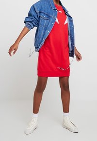 Punainen hupparimekko valkoisilla yksityiskohdilla, denim-takin alla. Yhdistetty valkoisiin korkeatoppaisiisiin tennareihin ja polvipituisille valkoisille sukille.