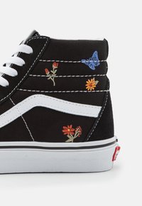 Baskets montantes noires avec lacets blancs et une bande blanche. Ornées d'une broderie colorée de fleurs et de papillons sur les côtés. Semelle en caoutchouc.