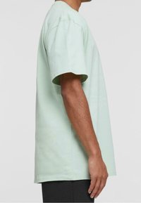 Jasnozielona koszulka z krótkim rękawem o luźnym kroju i okrągłym dekoltem, wykonana z miękkiej bawełny, zaprezentowana z boku.