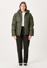 Oliven grøn pufferjakke med hætte, featuring lynlåslukning og quiltet design. Kombineret med sorte lige bukser og sorte sko.