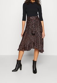 Czarna spódnica w wzory z falbaniastym dołem, z zaznaczeniem w pasie w formie węzła. Połączona z czarnymi botkami za kostkę. Długi rękaw czarnej bluzki.