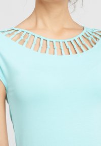 Top de color azul claro con un escote redondeado, detalles tejidos y acentos de nudos. Textura suave con mangas cortas.