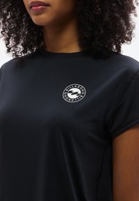 Μαύρο αθλητικό μπλουζάκι με κοντά μανίκια, με στρογγυλό λογότυπο σε άσπρο. Λείο ύφασμα με ραφές και άνετη γραμμή.