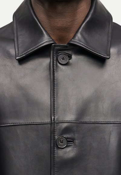 Κοντινό πλάνο ενός ατόμου που φοράει μαύρο δερμάτινο μπουφάν με ορατό γιακά και δύο μαύρα κουμπιά δεμένα μπροστά.