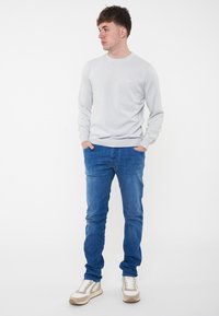 Felpa grigia chiara a maniche lunghe con scollatura rotonda, abbinata a jeans in denim blu e sneakers beige con accenti crema e suole testurizzate.