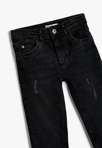 Jeans de mezclilla negra con un corte ajustado, que presentan un diseño desgastado y un ligero desvanecimiento. Detallados con bolsillos estándar y un cierre con botón metálico.