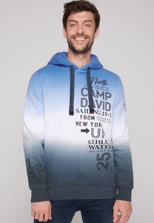 Sudadera con capucha en degradado azul a blanco, con cordones y detalles de texto impresos. Corte estándar con puños y dobladillo acanalado.