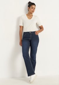 Mörkblå denimjeans med rak passform, ljusa sömmar och framfickor, kombinerat med en kortärmad vit V-ringad topp och vita sneakers.