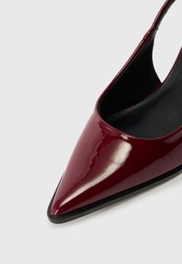 Burgundské lakované lodičky na podpatku se špičatou špičkou, hladkým povrchem a černým interiérem. Žádné viditelné kovové prvky nebo ozdoby.