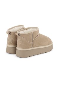 Botines de ante color topo con un interior suave, que cuentan con una cinta de color claro y una suela texturizada para mayor agarre. Tira en la parte trasera para ponerlos con facilidad.