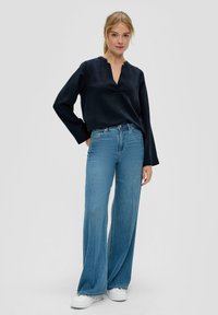 Marineblauwe blouse met lange mouwen en een V-hals, gecombineerd met lichtblauwe wijde denim jeans en witte sneakers. Gladde stof en een relaxte pasvorm.