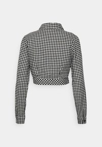 Veste courte à manches longues à carreaux noir et blanc avec un col et des poignets boutonnés, vue de dos.