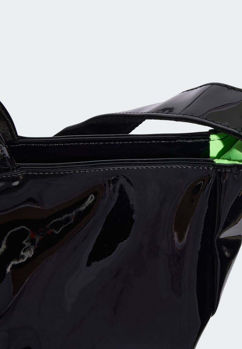 Bolso de charol negro con un acabado brillante, que presenta un interior verde y asas negras resistentes. Forma aerodinámica con cierre de cremallera.