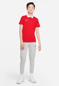Rode polo met een witte kraag en het Nike-logo, gecombineerd met grijze cargo-joggers met zakken en witte sneakers. Gelaagde stof.