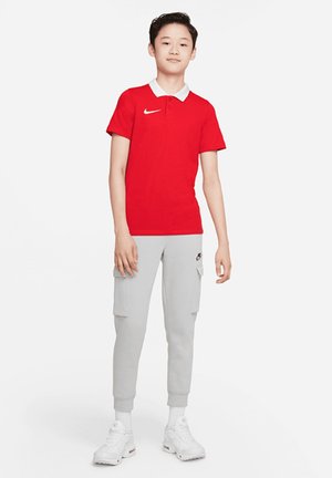 Rotes Polohemd mit weißem Kragen und Nike-Logo, kombiniert mit grauen Cargo-Jogginghosen mit Taschen und weißen Sneakers. Texturiertes Material.