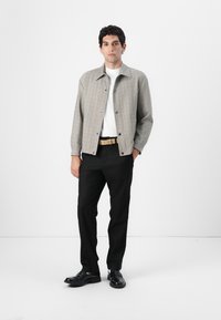 Szary w kratkę żakiet z kołnierzykiem, noszony na białej koszulce. Czarne spodnie i czarne buty dopełniają outfit.