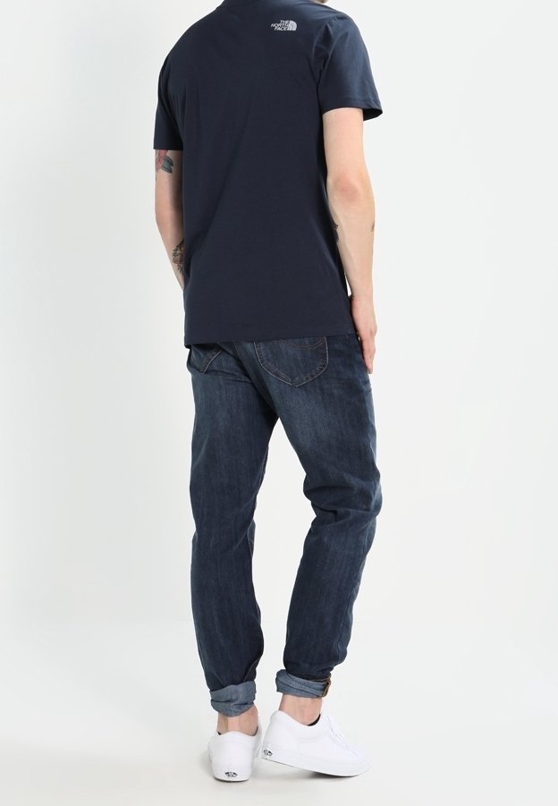 Merinavyinen puuvillat-paita, jossa on logo selässä, yhdistetty tummansinisiin farkkuihin ja valkoisiin tennareihin. Rennon mallinen, jossa on käännetyt hihansuut.