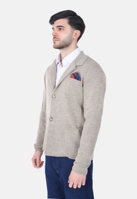 Cardigan beige realizzato in tessuto testurizzato, con rever a scanno, due bottoni e una tasca frontale con un fazzoletto colorato a motivi.