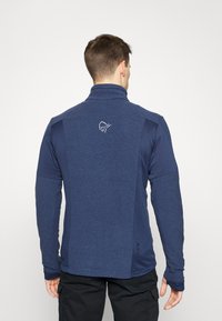 Marineblå glidelås-pullover laget av teksturert stoff, med lange ermer og en logo på øvre rygg.