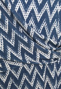 Tissu à motif zigzag bleu et blanc, avec une texture douce et des sections drapées, créant une profondeur visuelle et du mouvement.