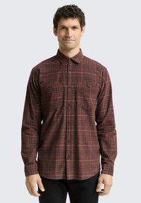 Chemise à manches longues à carreaux dans des tons de rouge foncé et de marron. Dotée de deux poches poitrine, d'une fermeture à boutons sur le devant et d'un col classique.