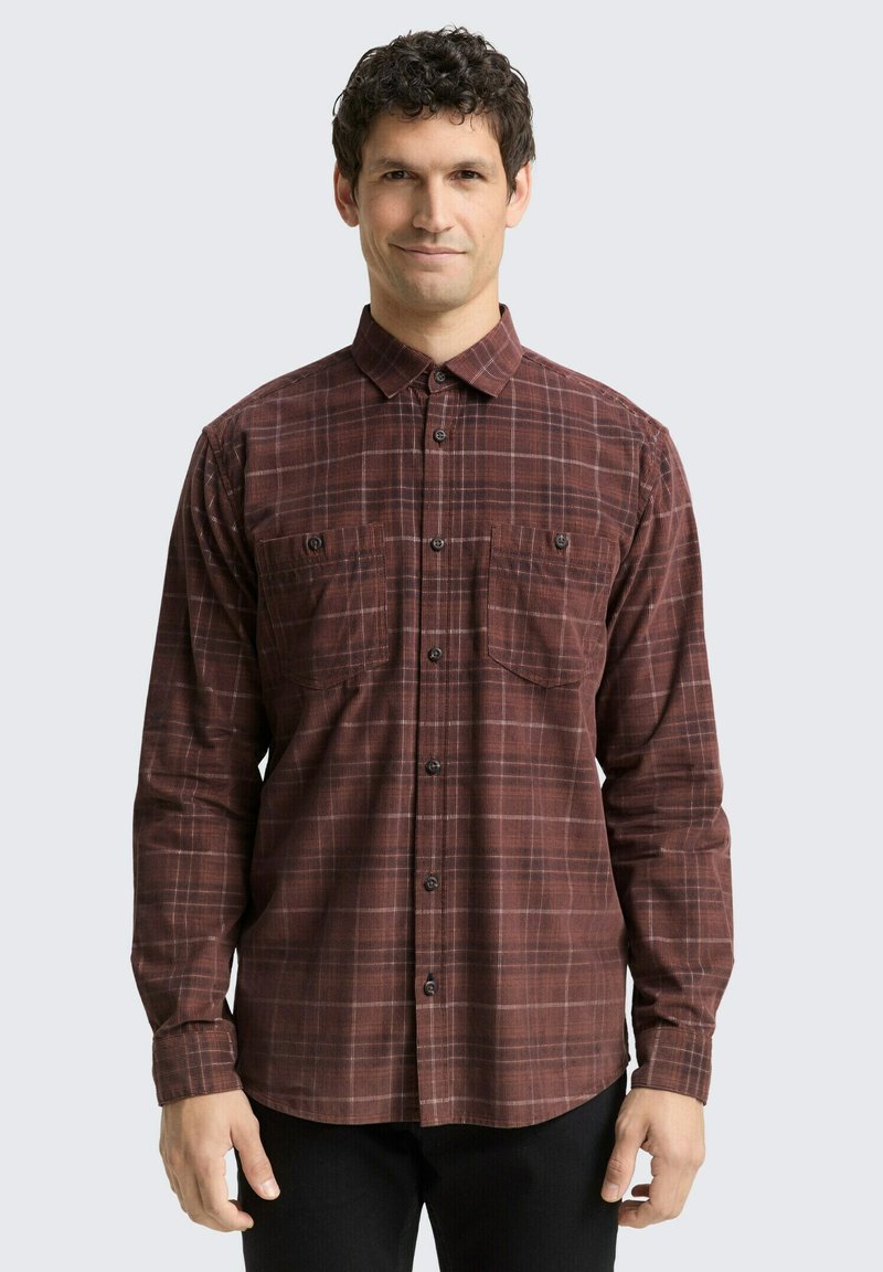 Chemise à manches longues à carreaux dans des tons de rouge foncé et de marron. Dotée de deux poches poitrine, d'une fermeture à boutons sur le devant et d'un col classique.