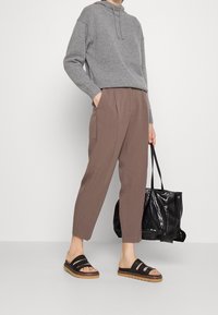 Szara dzianinowa bluza z kapturem, brązowe zwężane spodnie, czarne klapki na trzy paski oraz czarna błyszcząca torba typu tote. Gładkie faktury na całej powierzchni.