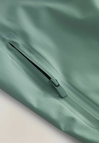 Material mint verde rezistent la apă cu un fermoar ascuns. Textură netedă, design elegant și detalii minime. Ideal pentru utilizare în aer liber.
