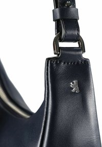 Close-up van een donkerblauwe leren handtasriem met een zilveren berenembleem en metalen hardware op een witte achtergrond.