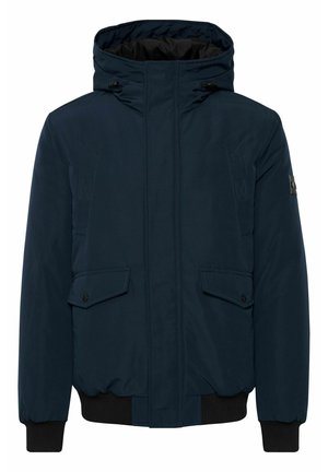 Veste matelassée bleu marine avec capuche, ouverture zippée, deux poches à rabat à l'avant et poignets côtelés. Présente un accent de logo sur la manche gauche.