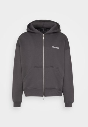 Ciemnoszara bluza z kapturem na zamek błyskawiczny, z przednimi kieszeniami i małym białym logo „WRSTBHVR” na lewej piersi.